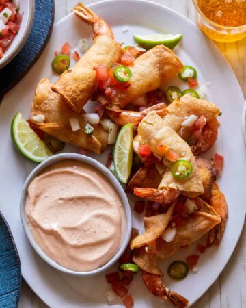 A platter of shrimp taquitos with lime wedges and creamy chipotle sauce on the side.