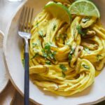 A bowl of Thai yellow curry noodles with shiitake mushrooms and a fork.