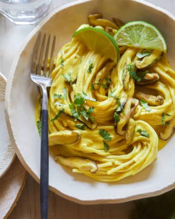 A bowl of Thai yellow curry noodles with shiitake mushrooms and a fork.