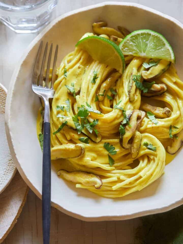 A bowl of Thai yellow curry noodles with shiitake mushrooms and a fork.