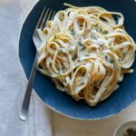 Roasted garlic vegan fettuccine alfredo on a blue plate with a fork.