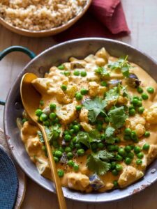 A pan of vegetable loaded vegan korma with a wooden spoon.