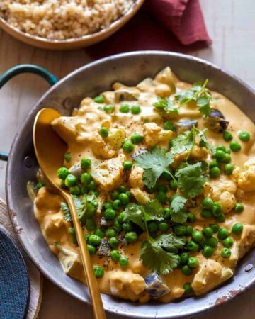 A pan of vegetable loaded vegan korma with a wooden spoon.