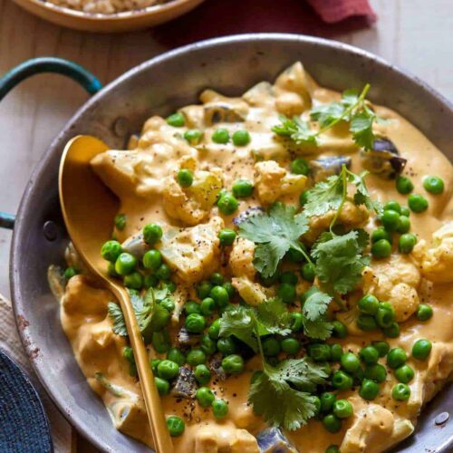 A pan of vegetable loaded vegan korma with a wooden spoon.