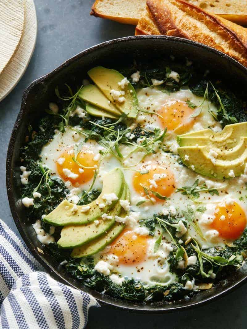An image of Green Shakshuka in a skillet with bread in the background. 