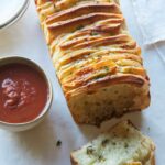 A close up of cheesy pull apart bread with sauce on the side.