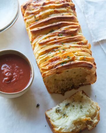 A close up of cheesy pull apart bread with sauce on the side.
