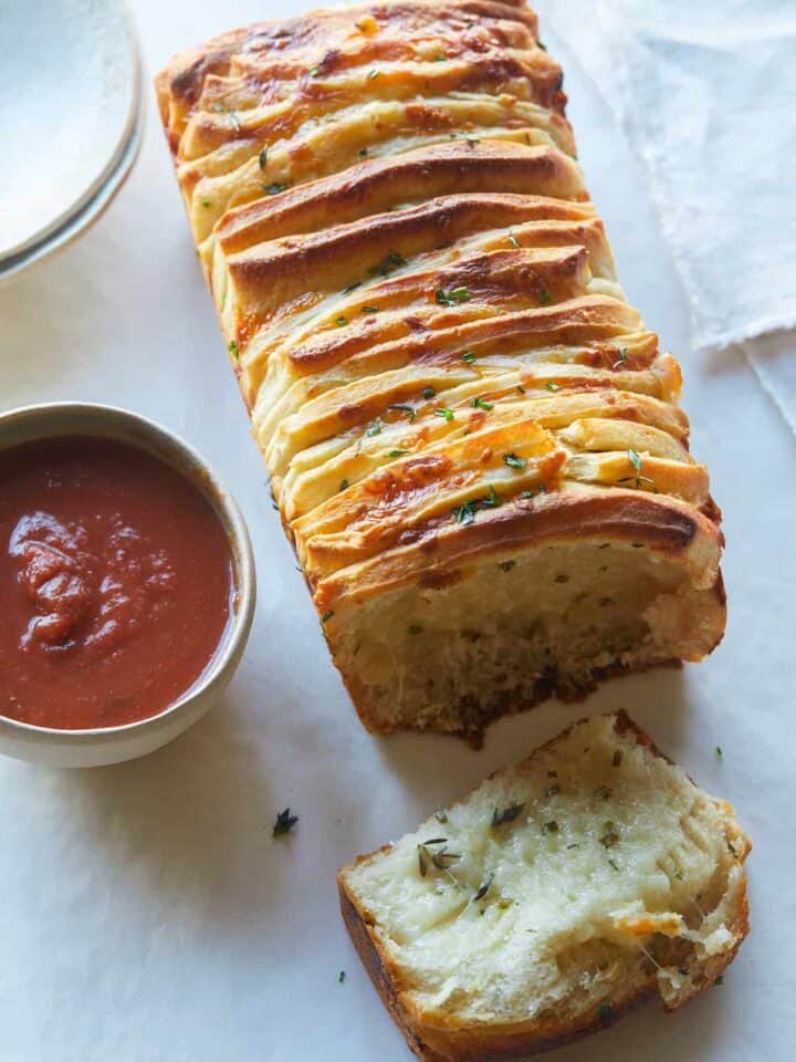 A close up of cheesy pull apart bread with sauce on the side.