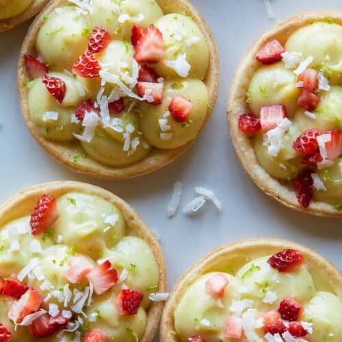 A close up of coconut lime tarts topped with sugar soaked strawberries.