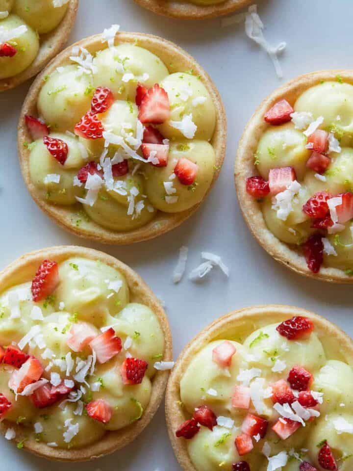 A close up of coconut lime tarts topped with sugar soaked strawberries.