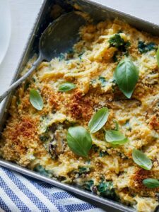 A close up of creamy vegan spaghetti squash, wild mushroom, and spinach bake with a spoon.