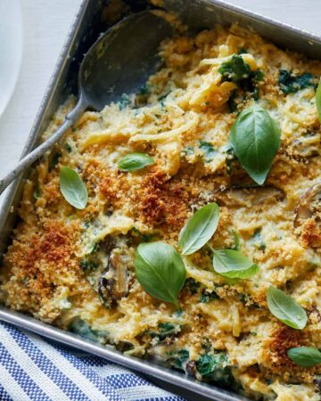 A close up of creamy vegan spaghetti squash, wild mushroom, and spinach bake with a spoon.
