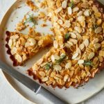 A sliced almond and honey cornmeal cake with a knife.