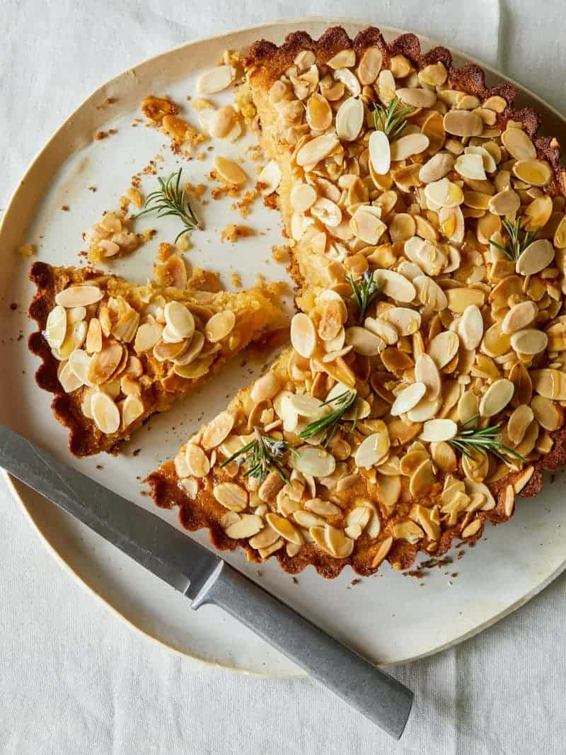 Sliced almond honey cornmeal cake with a piece taken out and a knife on the plate.