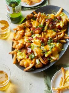 A plate of breakfast poutine with hollandaise sauce and drinks.