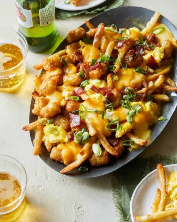 A plate of breakfast poutine with hollandaise sauce and drinks.