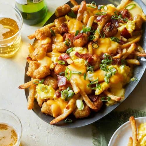 A plate of breakfast poutine with hollandaise sauce and drinks.