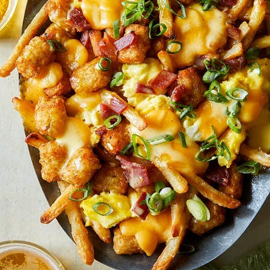 Breakfast poutine recipe in an oval dish with a beer next to it. 
