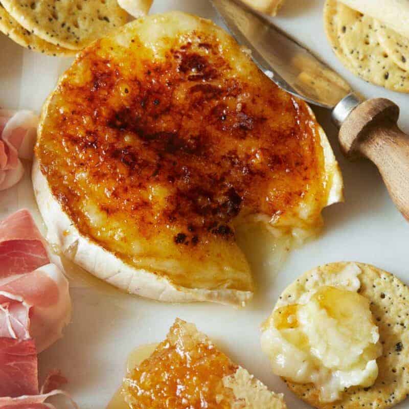 A close up of honey brûlée brie with crackers, meat, and cheese knife, a new years eve appetizer recipe.