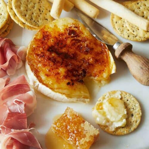 Honey brûlée brie with crackers, meat, and cheese knife, a popular Thanksgiving appetizer.