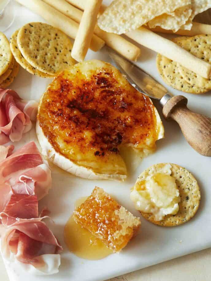 Honey brûlée brie with crackers, meat, and cheese knife, a popular appetizer recipe. 