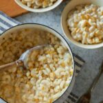 A pot and bowls of creamed corn mac and cheese with a serving spoon.