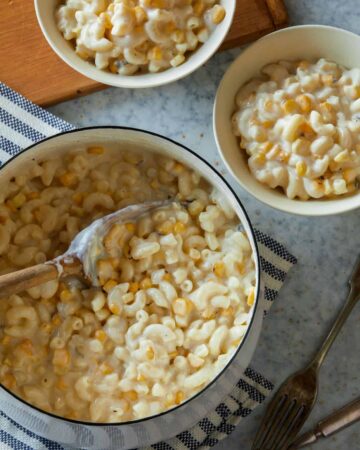 A pot and bowls of creamed corn mac and cheese with a serving spoon.