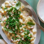 Creamy baked gnocchi with ham and peas and a serving spoon.