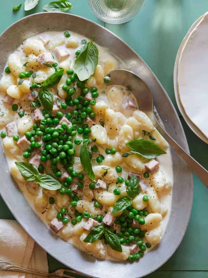 Creamy baked gnocchi with ham and peas and a serving spoon.