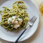 A plate of English pea, basil, and pistachio pesto linguine with burrata and a fork.