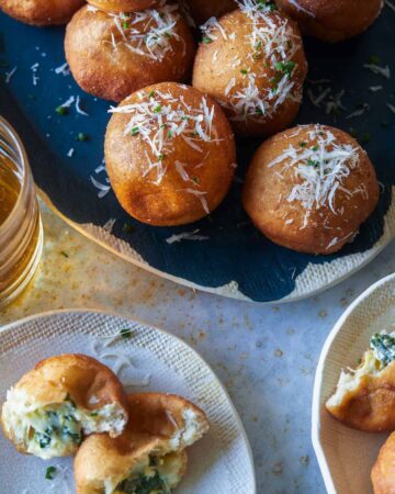 A platter of spinach and artichoke stuffed beignets and servings on small plates.