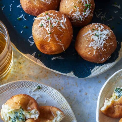 A platter of spinach and artichoke stuffed beignets and servings on small plates.