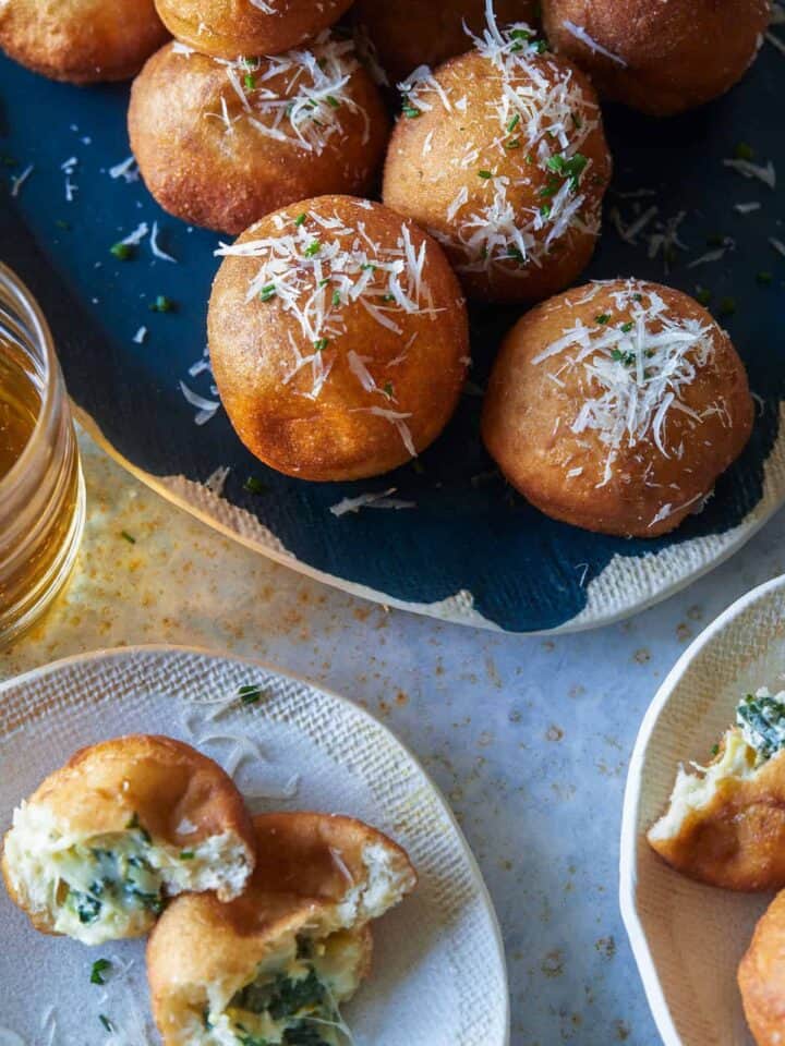 A platter of spinach and artichoke stuffed beignets and servings on small plates.