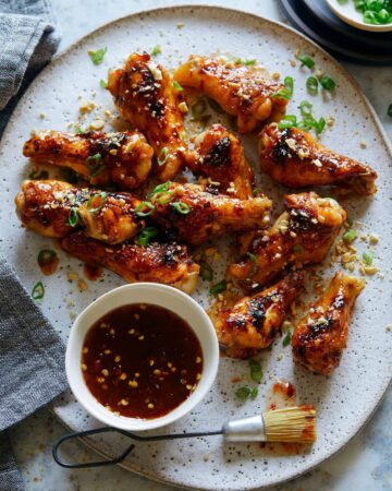 A plate of sticky honey, garlic and chile glazed chicken drumlettes with a bowl of sauce.