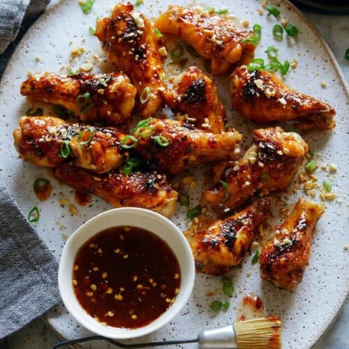 A plate of sticky honey, garlic and chile glazed chicken drumlettes with a bowl of sauce.