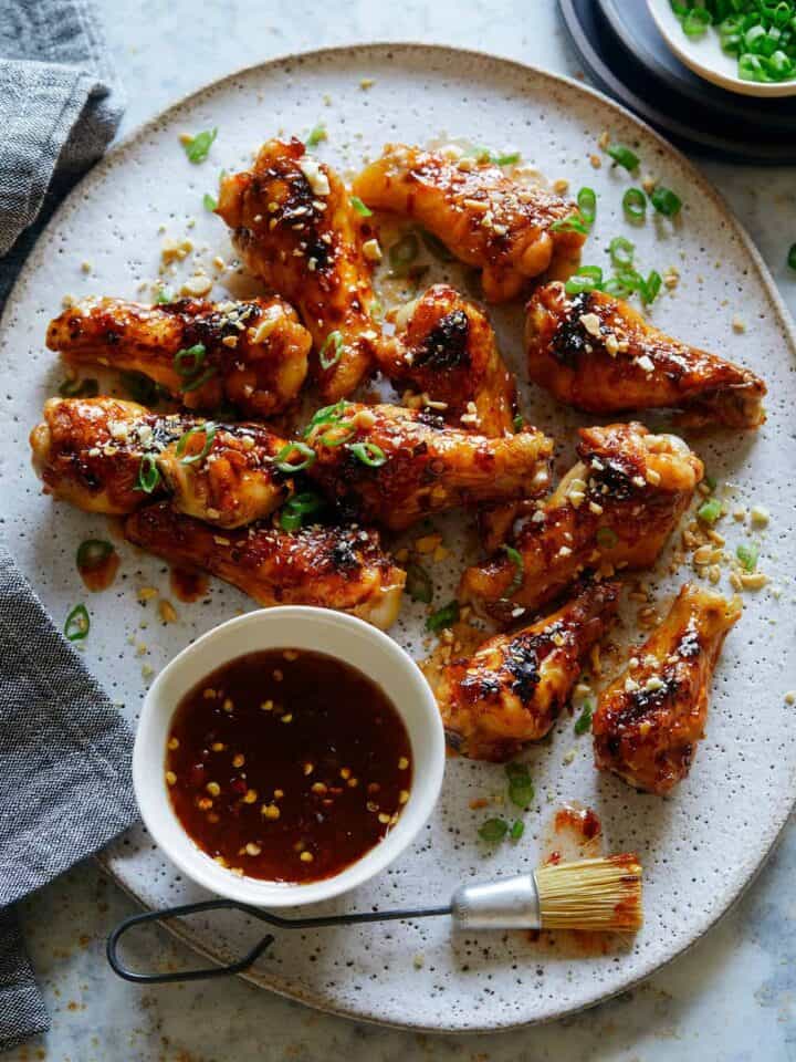 A plate of sticky honey, garlic and chile glazed chicken drumlettes with a bowl of sauce.