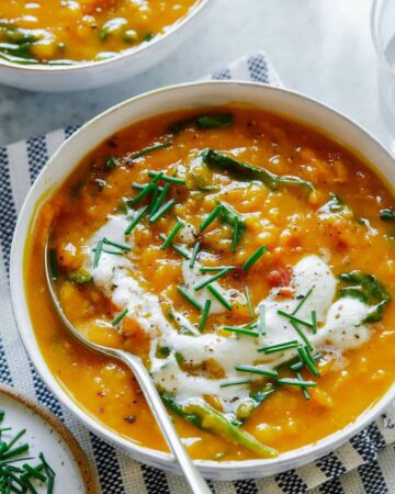 A bowl of vegan lentil and spinach soup topped with garlicky almond cream and a spoon.