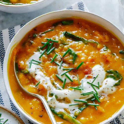 A bowl of vegan lentil and spinach soup topped with garlicky almond cream and a spoon.