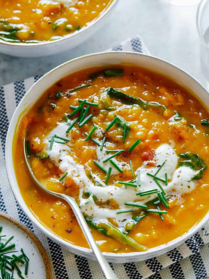 A bowl of vegan lentil and spinach soup topped with garlicky almond cream and a spoon.