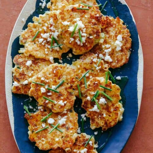 Corn cakes with chives and queso fresco on blue and white platter.