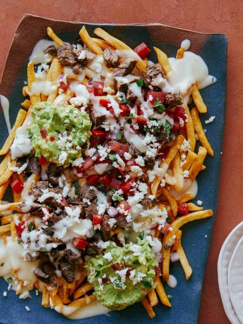A blue platter of carne asada fries with small plates.