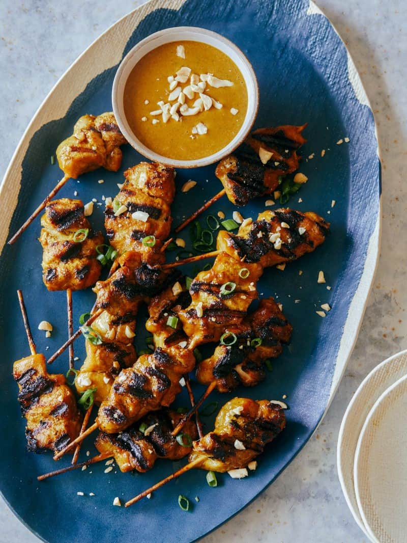 Chicken satay with peanut sauce on a blue platter.