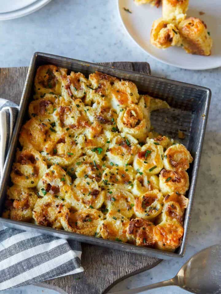 A square pan of savory french toast roll ups with some served on a small plate.