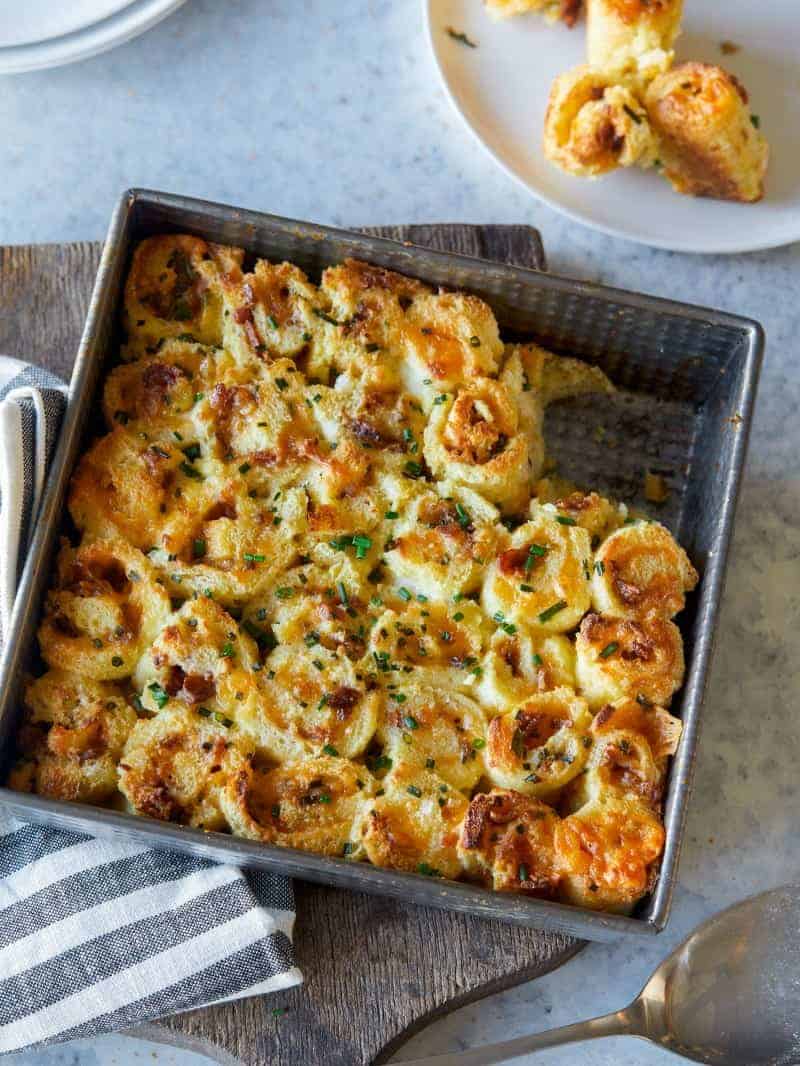 Savory french toast roll ups in a baking dish with some scooped out on a plate. 