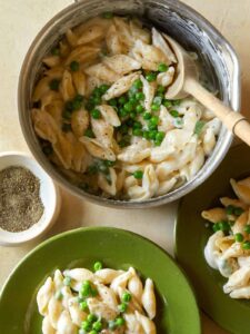 A bowl of white cheddar mac, cheese, and sweet peas being served on plates.