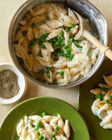 A bowl of white cheddar mac, cheese, and sweet peas being served on plates.