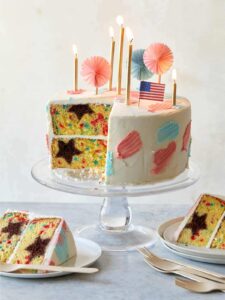 A sliced and partially served 4th of July funfetti cake with candles and flags.