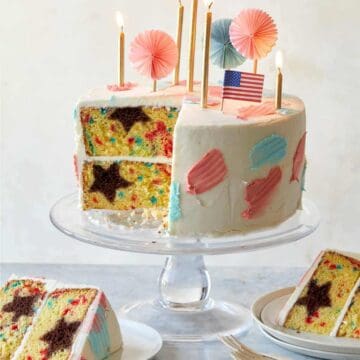A sliced and partially served 4th of July funfetti cake with candles and flags.
