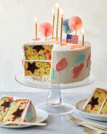 A sliced and partially served 4th of July funfetti cake with candles and flags.