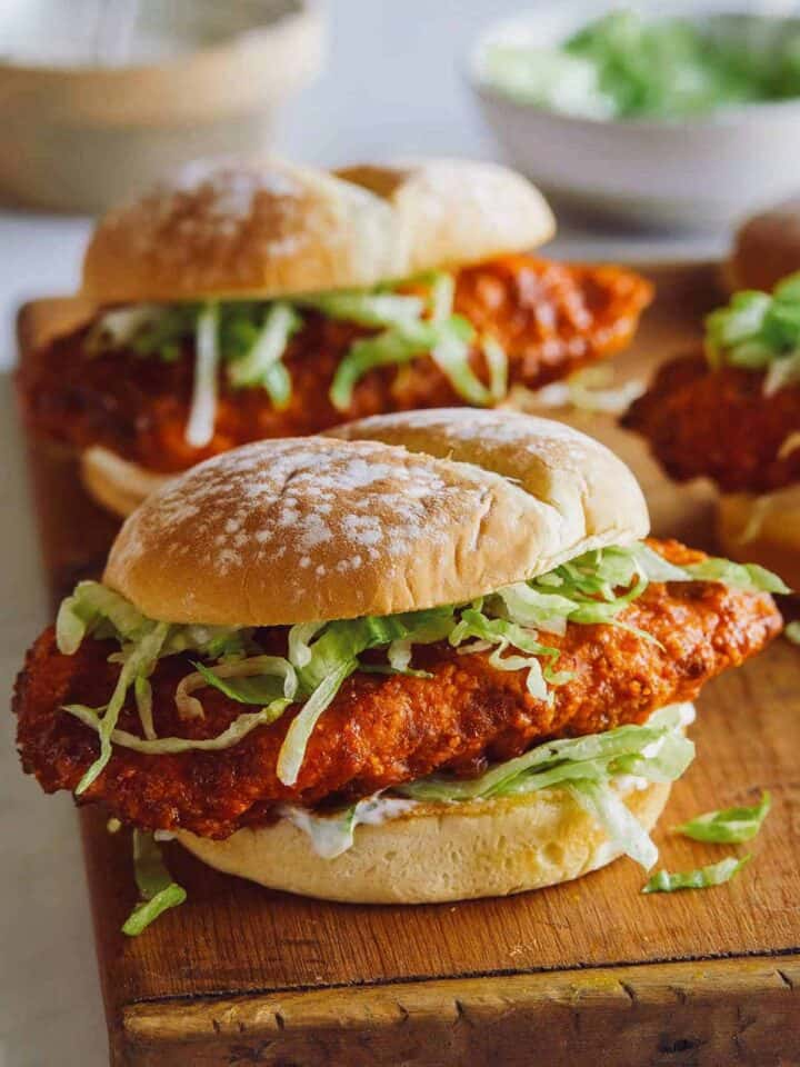 A close up of Nashville honey hot chicken sandwiches on a wooden cutting board.